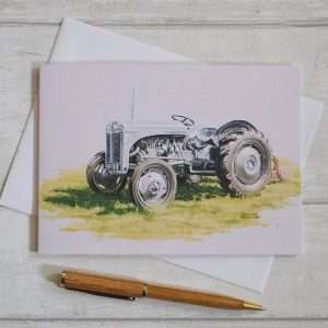 Grey Ferguson tractor art on a blank, oblong birthday card. Viewed flat from above on top of white envelope with pen in foreground for scale