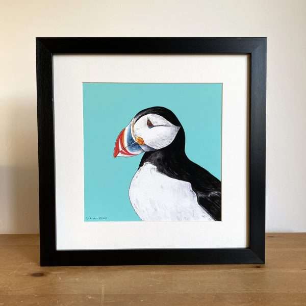 Puffin Black Frame scaled 10" x 10" art print of my original watercolour, fine liner and pencil illustration of a puffin on a blue background.