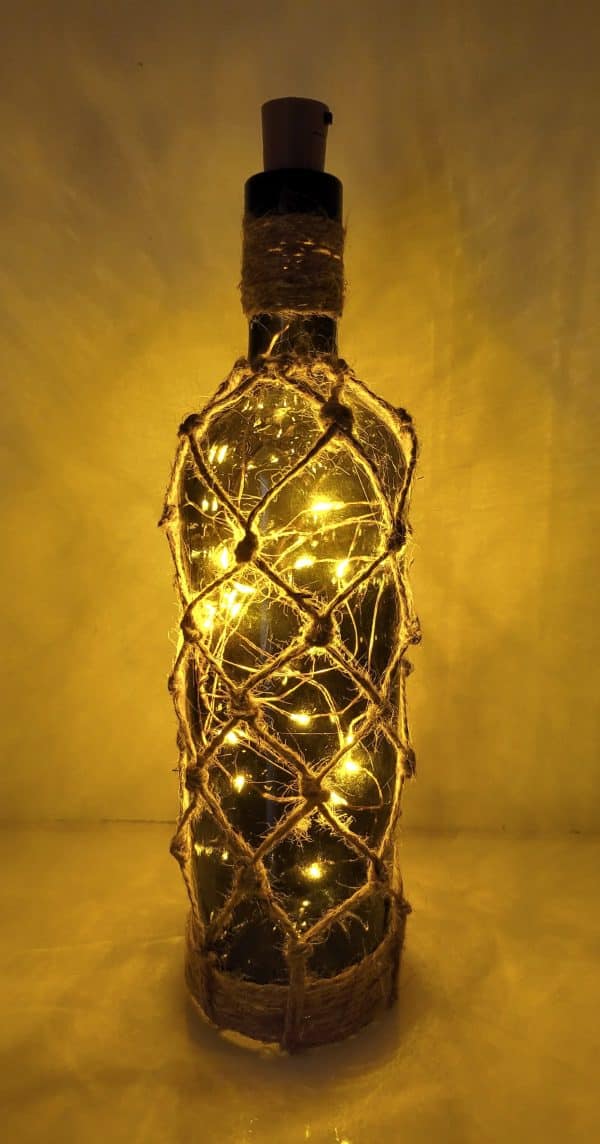 lit up green glass wine bottle with jute twine braiding in a diamond pattern. Jute twine wound down the bottle neck. Jute twine wound around the bottom of the bottle. Cork LED lights