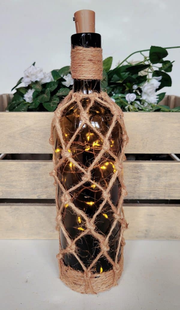 green glass wine bottle with jute twine braiding in a diamond pattern. Jute twine wound down the bottle neck. Jute twine wound around the bottom of the bottle. Cork LED lights non lit