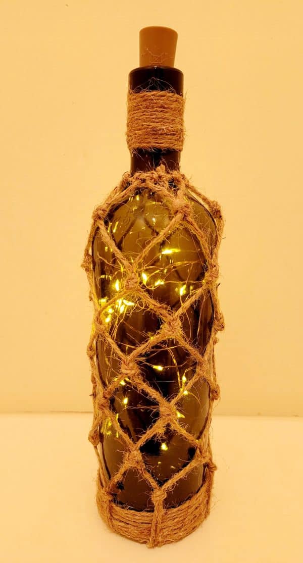 lit up green glass wine bottle with jute twine braiding in a diamond pattern. Jute twine wound down the bottle neck. Jute twine wound around the bottom of the bottle. Cork LED lights