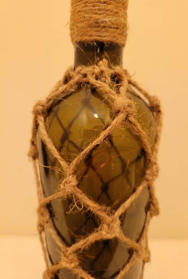 top half of a green glass wine bottle. Jute twine detailing in a diamond pattern. Twine wrapped around the neck of the bottle
