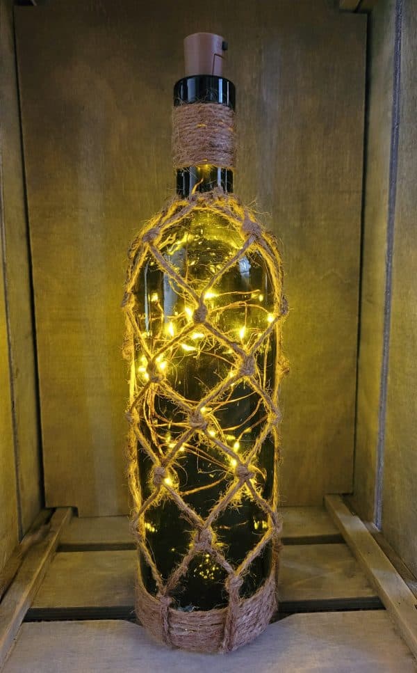 lit up green glass wine bottle with jute twine braiding in a diamond pattern. Jute twine wound down the bottle neck. Jute twine wound around the bottom of the bottle. Cork LED lights